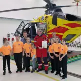 Dzieci w pomarańczowych koszulkach i dorośli pozują przed żółto-czerwonym helikopterem HEMS. Pomocna ekipa PGNiG z pewnością doceniła tę wizytę.