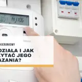 Dłoń wskazuje na licznik dwukierunkowy, pokazując jego odczyty. Dowiedz się, jak działa i jak odczytać wskazania licznika dwukierunkowego.