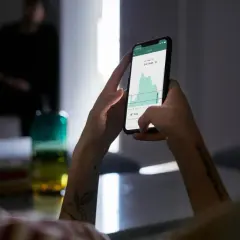 Ręce trzymające smartfon z wykresem cen energii. Aplikacja pokazuje fakturę za energię, pomagając zarządzać wydatkami.