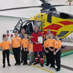 Dzieci w pomarańczowych koszulkach i dorośli pozują przed żółto-czerwonym helikopterem HEMS. Pomocna ekipa PGNiG z pewnością doceniła tę wizytę.