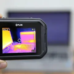 Ręczny termograf FLIR pokazuje laptopa w podczerwieni. Widoczne są różne temperatury, od chłodniejszych fioletów po cieplejsze żółcie i róże.