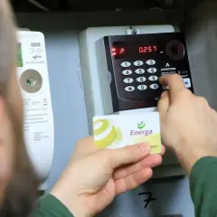 Osoba wprowadza kod na liczniku przedpłatowym, by opłacić stałe opłaty za energię. Karta Energa w dłoni.