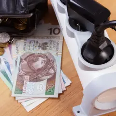 Portfel z pieniędzmi i monety obok listwy zasilającej. Rosnące ceny prądu to spory dodatek do rachunków.