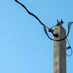 Betonowy słup na działce, który stoi tam od ponad 30 lat, z plątaniną kabli elektrycznych na tle błękitnego nieba.