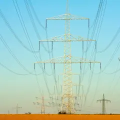 Linie energetyczne na tle błękitnego nieba. Wiele słupów wysokiego napięcia, tworzących sieć, jakby ilustrowało przelicznik MW na KW.