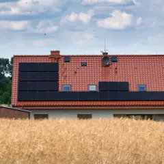 Dom z panelami słonecznymi na dachu, otoczony polem zboża. Może to być znak, że nawet w takich miejscach jest za wysokie napięcie w sieci.