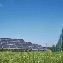 Panele słoneczne na zielonej łące, w tle niebieskie niebo. Trwa budowa falownika, który zamieni energię słoneczną na prąd.