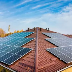 Dach pokryty brązową dachówką z zainstalowanymi panelami fotowoltaicznymi. Widać kilka rzędów ogniw monokrystalicznych, które zbierają energię słoneczną.