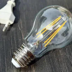 Żarówka LED i biała wtyczka na ciemnym drewnianym tle. Symbolizują potencjał, który czeka na aktywację, jak współczynnik jednoczesności w technologii.