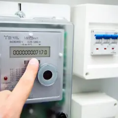 Palec wskazuje licznik energii elektrycznej Apator Norax 3, na którym widnieje odczyt 00000000717.0. Obok znajduje się skrzynka z bezpiecznikami.