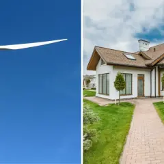 Biała elektrownia wiatrowa na tle błękitnego nieba obok nowoczesnego domu z zielonym trawnikiem.