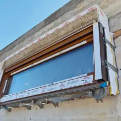Montaż okna z warstwą termoizolacji, widoczne materiały izolacyjne i profile okienne.