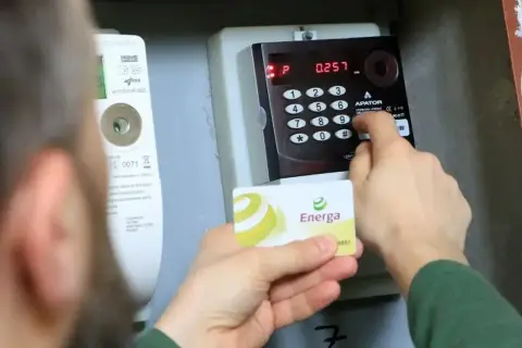 Osoba wprowadza kod na liczniku przedpłatowym, by opłacić stałe opłaty za energię. Karta Energa w dłoni.