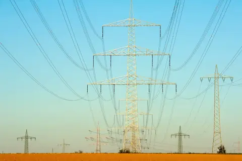 Linie energetyczne na tle błękitnego nieba. Wiele słupów wysokiego napięcia, tworzących sieć, jakby ilustrowało przelicznik MW na KW.
