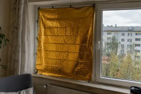 Złoty koc termiczny na okno, chroniący przed zimnem. W tle widać budynek mieszkalny i drzewa.
