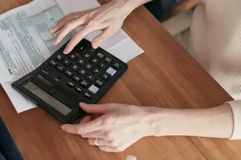 Ręce liczą na kalkulatorze przy dokumentach podatkowych. Dowiedz się, jak zrezygnować z opłaty handlowej PGE.