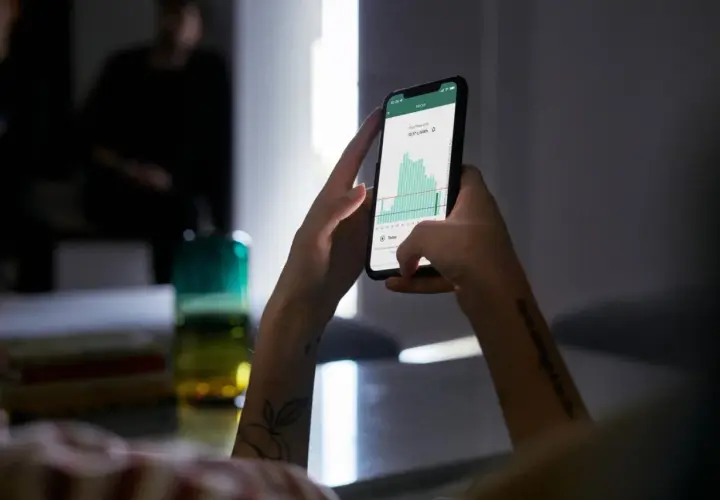 Ręce trzymające smartfon z wykresem cen energii. Aplikacja pokazuje fakturę za energię, pomagając zarządzać wydatkami.