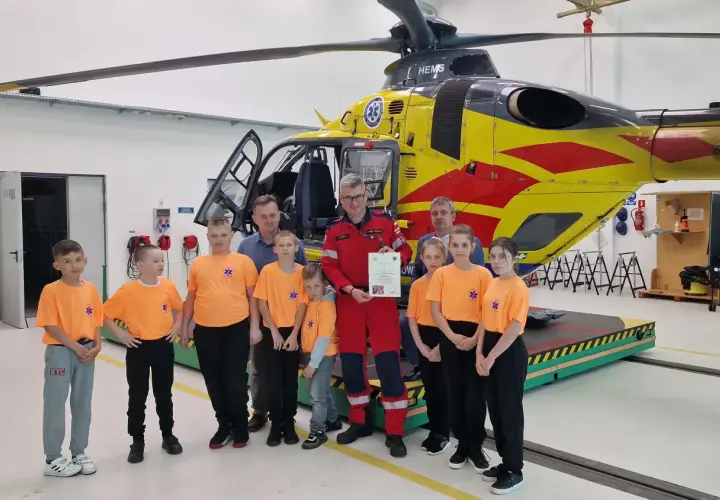 Dzieci w pomarańczowych koszulkach i dorośli pozują przed żółto-czerwonym helikopterem HEMS. Pomocna ekipa PGNiG z pewnością doceniła tę wizytę.