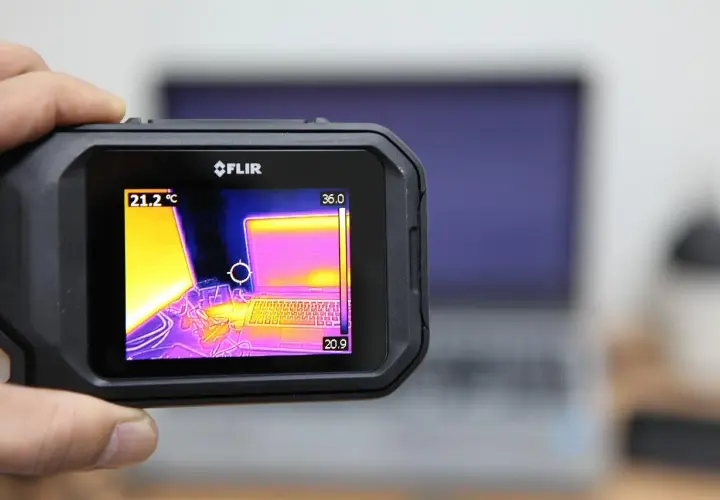 Ręczny termograf FLIR pokazuje laptopa w podczerwieni. Widoczne są różne temperatury, od chłodniejszych fioletów po cieplejsze żółcie i róże.