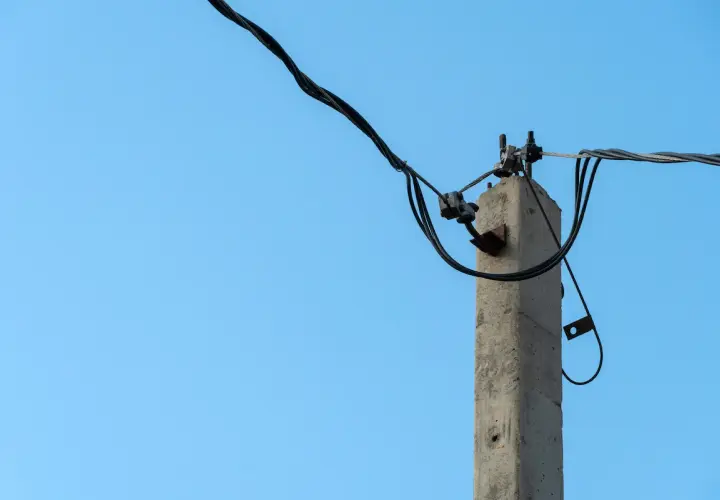 Betonowy słup na działce, który stoi tam od ponad 30 lat, z plątaniną kabli elektrycznych na tle błękitnego nieba.