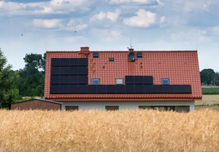 Dom z panelami słonecznymi na dachu, otoczony polem zboża. Może to być znak, że nawet w takich miejscach jest za wysokie napięcie w sieci.