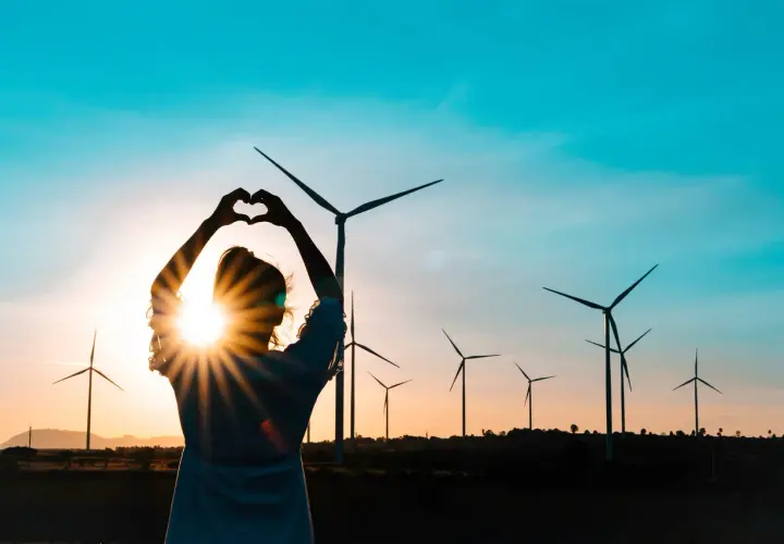 Sylwetka kobiety tworzy serce na tle zachodzącego słońca i farmy wiatrowej. Miłość do czystych źródeł energii.