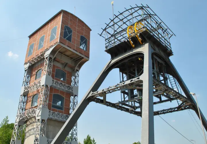 Dwie wieże kopalniane, jedna ceglana, druga metalowa z kołem, tworzą futurystyczny grawitacyjny magazyn energii.