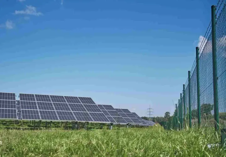 Panele słoneczne na zielonej łące, w tle niebieskie niebo. Trwa budowa falownika, który zamieni energię słoneczną na prąd.