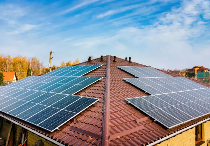 Dach pokryty brązową dachówką z zainstalowanymi panelami fotowoltaicznymi. Widać kilka rzędów ogniw monokrystalicznych, które zbierają energię słoneczną.