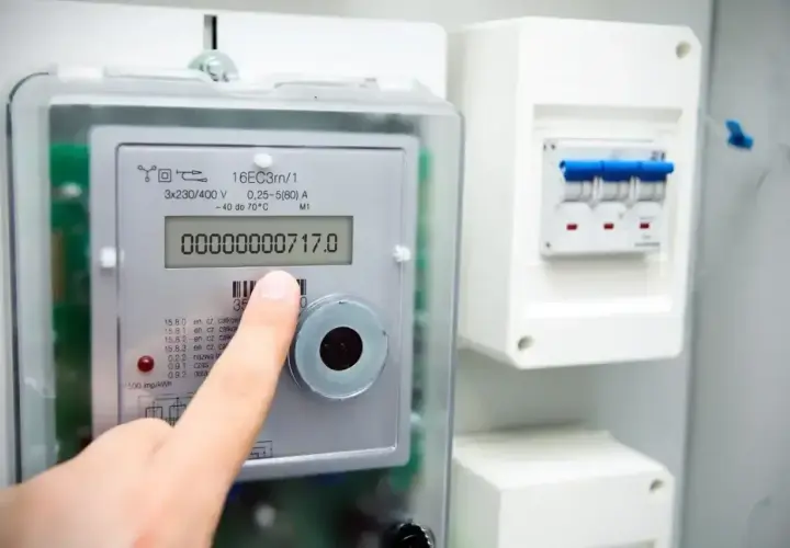 Palec wskazuje licznik energii elektrycznej, na którym widnieje odczyt 717.0. Obok znajduje się skrzynka z bezpiecznikami.