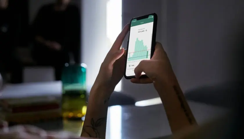 Ręce trzymające smartfon z wykresem cen energii. Aplikacja pokazuje fakturę za energię, pomagając zarządzać wydatkami.
