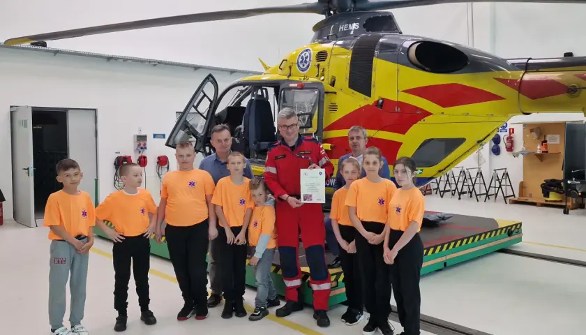 Dzieci w pomarańczowych koszulkach i dorośli pozują przed żółto-czerwonym helikopterem HEMS. Pomocna ekipa PGNiG z pewnością doceniła tę wizytę.