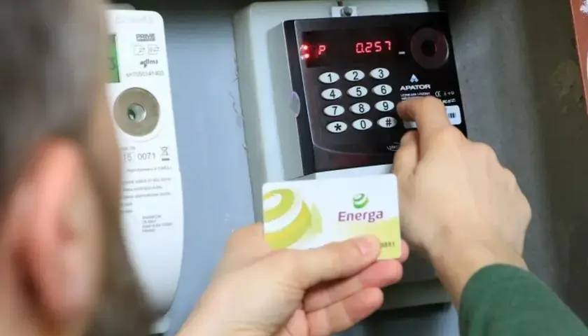 Osoba wprowadza kod na liczniku przedpłatowym, by opłacić stałe opłaty za energię. Karta Energa w dłoni.