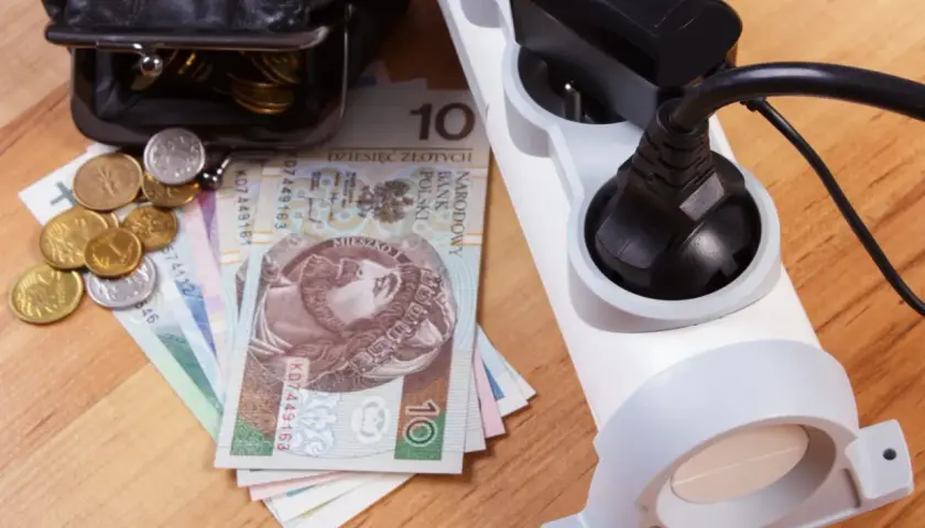 Portfel z pieniędzmi i monety obok listwy zasilającej. Rosnące ceny prądu to spory dodatek do rachunków.