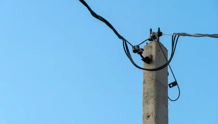 Betonowy słup na działce, który stoi tam od ponad 30 lat, z plątaniną kabli elektrycznych na tle błękitnego nieba.
