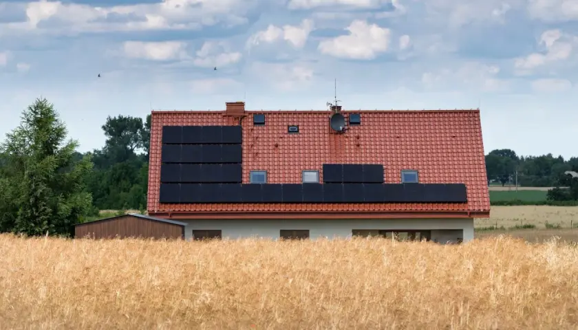 Dom z panelami słonecznymi na dachu, otoczony polem zboża. Może to być znak, że nawet w takich miejscach jest za wysokie napięcie w sieci.