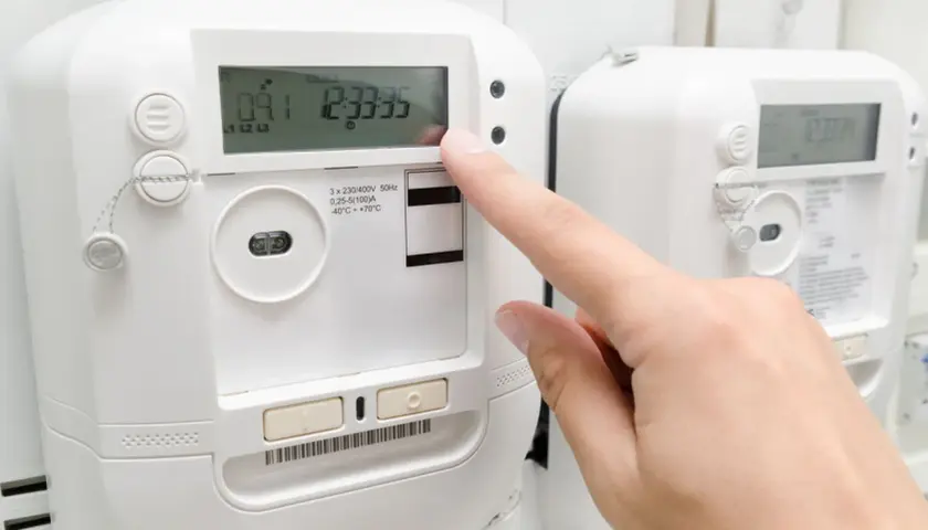 Palec naciska przycisk licznika energii elektrycznej, monitorując pobór prądu.