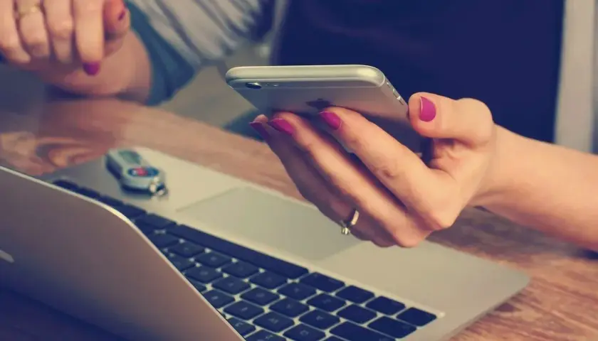 Kobieta z różowym lakierem na paznokciach trzyma telefon, obok laptopa. Szybko dzwoni na infolinię Energa Obrót, by rozwiązać sprawę.