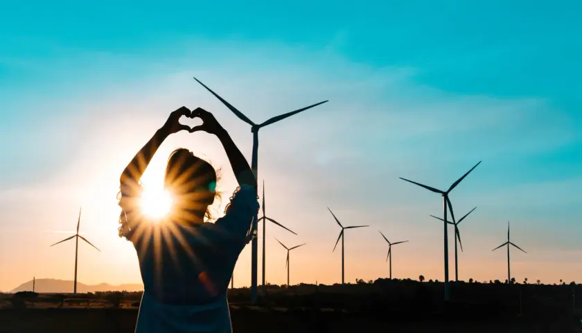 Sylwetka kobiety tworzy serce na tle zachodzącego słońca i farmy wiatrowej. Miłość do czystych źródeł energii.