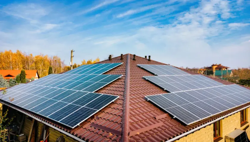 Dach pokryty brązową dachówką z zainstalowanymi panelami fotowoltaicznymi. Widać kilka rzędów ogniw monokrystalicznych, które zbierają energię słoneczną.