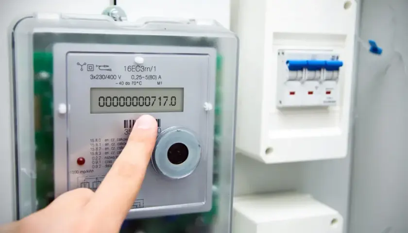 Palec wskazuje licznik energii elektrycznej Apator Norax 3, na którym widnieje odczyt 00000000717.0. Obok znajduje się skrzynka z bezpiecznikami.