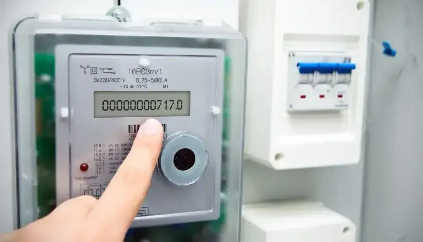 Palec wskazuje licznik energii elektrycznej, na którym widnieje odczyt 717.0. Obok znajduje się skrzynka z bezpiecznikami.