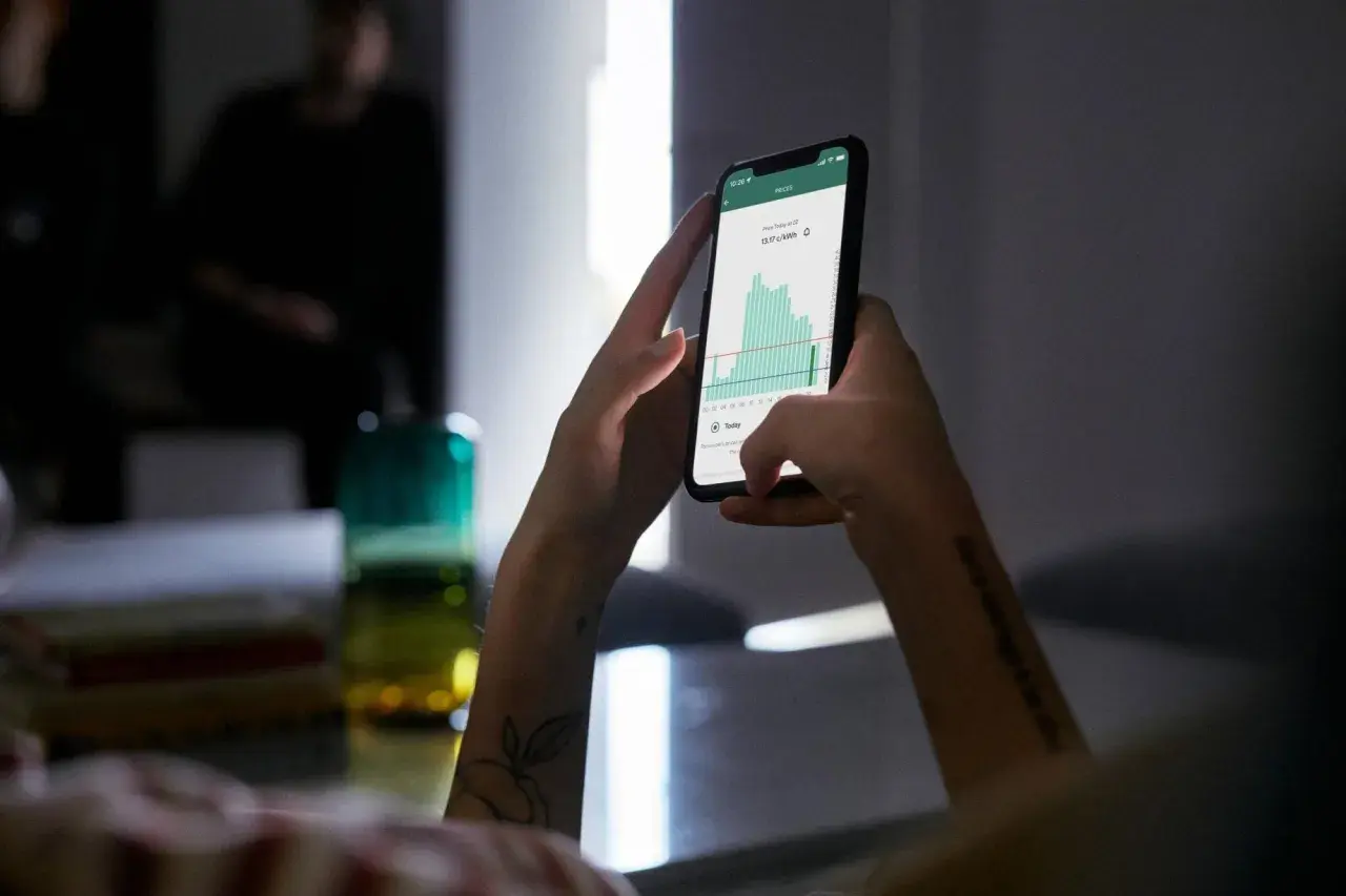 Ręce trzymające smartfon z wykresem cen energii. Aplikacja pokazuje fakturę za energię, pomagając zarządzać wydatkami.