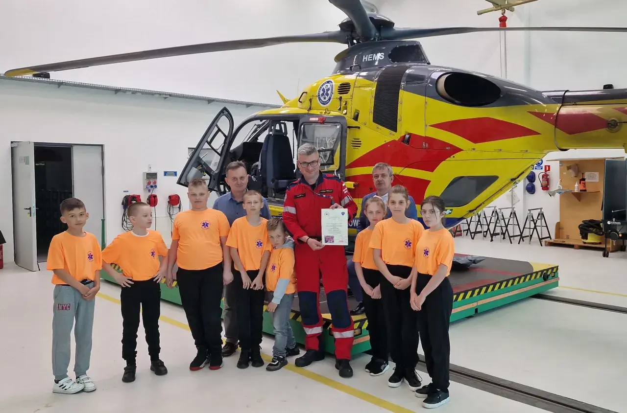 Dzieci w pomarańczowych koszulkach i dorośli pozują przed żółto-czerwonym helikopterem HEMS. Pomocna ekipa PGNiG z pewnością doceniła tę wizytę.