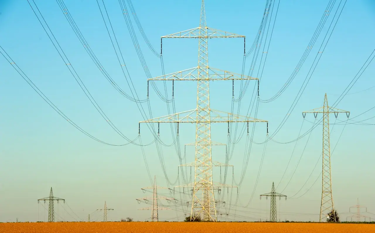 Linie energetyczne na tle błękitnego nieba. Wiele słupów wysokiego napięcia, tworzących sieć, jakby ilustrowało przelicznik MW na KW.
