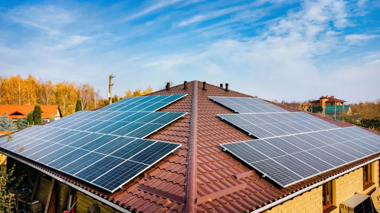 Dach pokryty brązową dachówką z zainstalowanymi panelami fotowoltaicznymi. Widać kilka rzędów ogniw monokrystalicznych, które zbierają energię słoneczną.